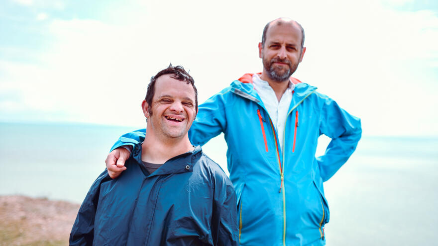 Two men stood together on the beach who are smiling and looking happy.