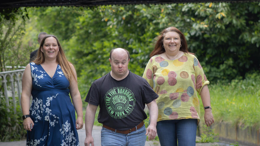 Two women walking either side of a man, smiling and laughing, as they stroll alongside a canal. 