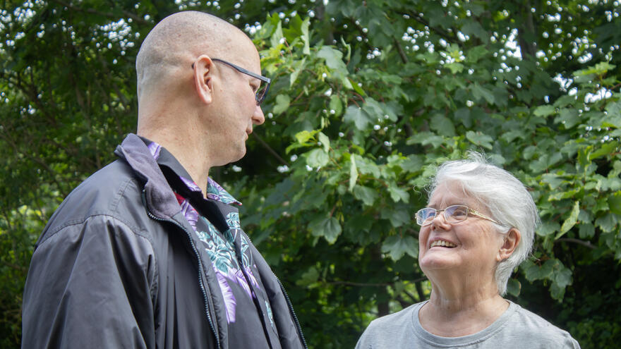 A woman looking up at her grown-up adult son with a smile who is standing next to her.