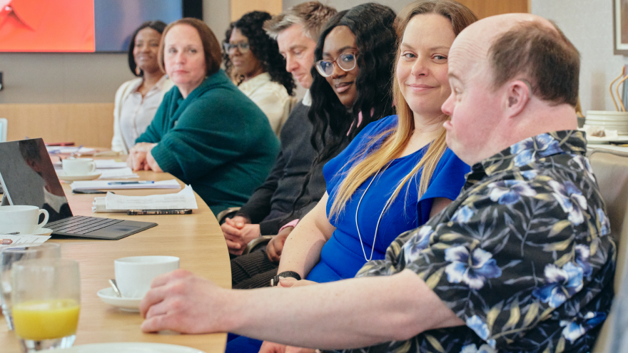 A man sat with members of the board and staff from Mencap Trust Company. He is talking and they are all listening and looking at him. 