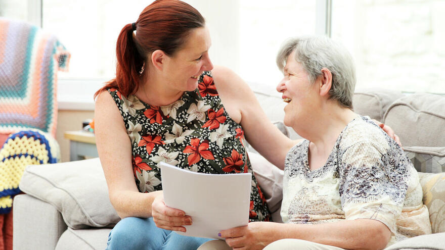 A carer sitting beside a women talking her through a document and offering her support. 