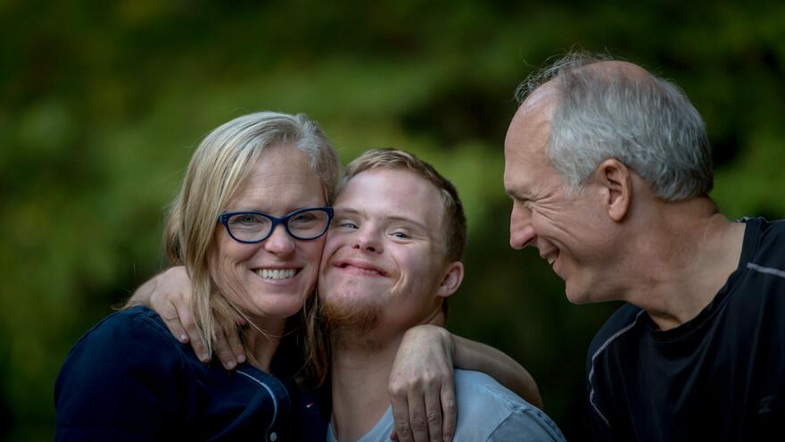 Parents proudly hugging and wrapping their arms around their son. 