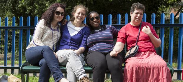 Group of people sat outside in sunshine on a bench in front of a playpark