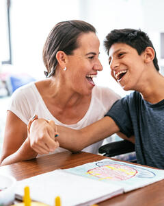 A woman supporting a boy with a learning disability who are both laughing and smiling together.  